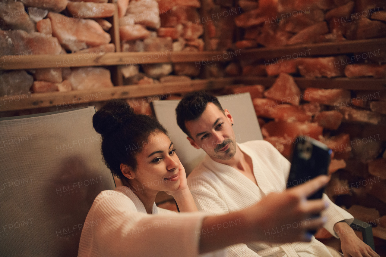 Portrait of happy young couple in salt inhalation steam room, taking selfie.