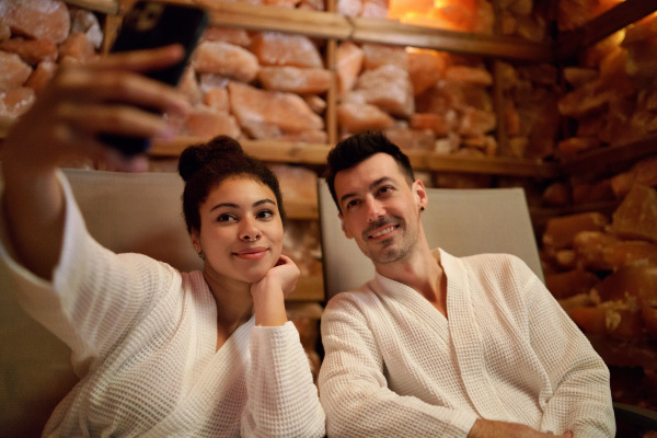 Portrait of happy young couple in salt inhalation steam room, taking selfie.