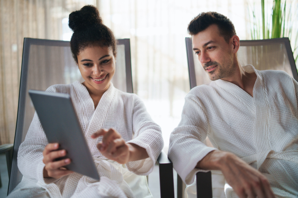 A portrait of young couple relaxing in spa resort, using tablet.