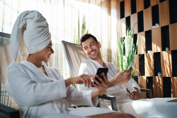 A portrait of young couple relaxing in spa resort, using smartphone.