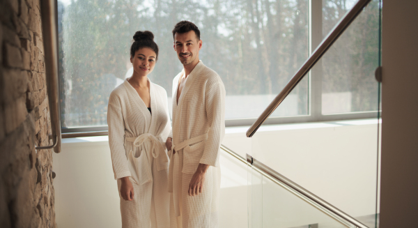 A portrait of young couple in spa resort, looking at camera on staircase.