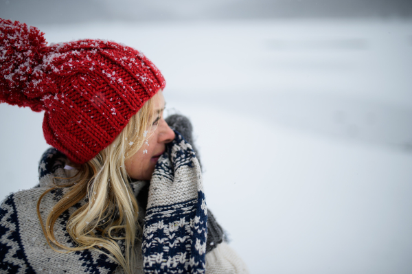 Portrait of happy senior woman with hat and mittens outdoors standing in snowy nature.