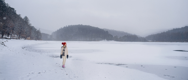 An active senior woman on walk outdoors in snowy nature, walking by frozen lake.