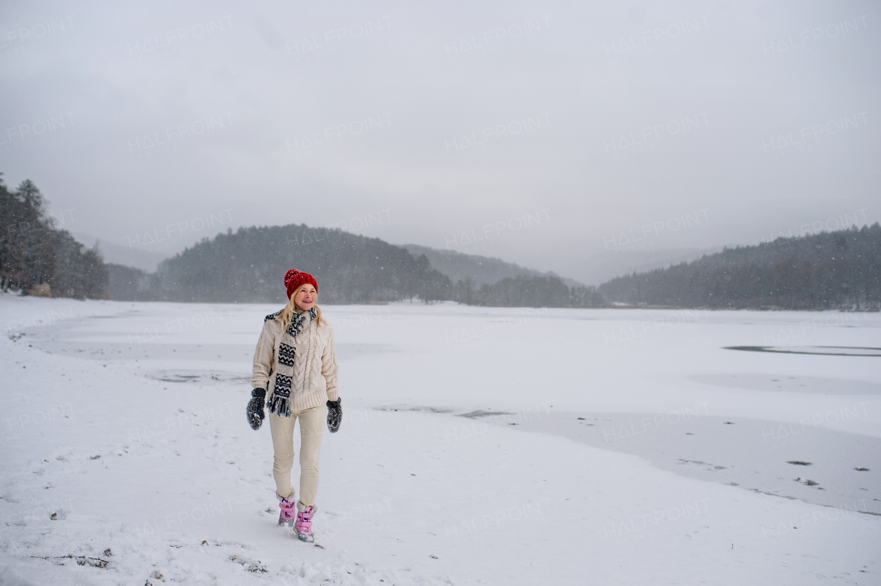 An active senior woman on walk outdoors in snowy nature, walking by frozen lake.