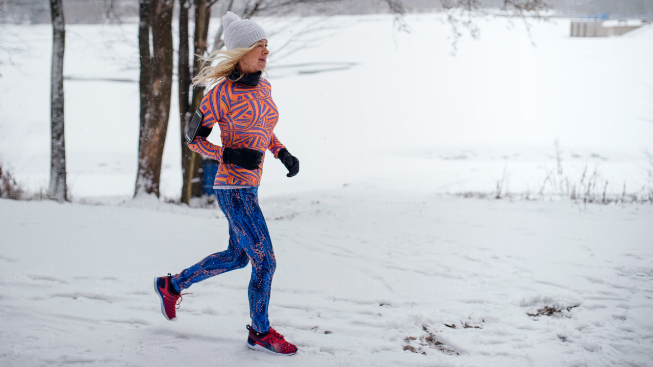 Side view of active senior woman running outdoors in winter, doing exercise.