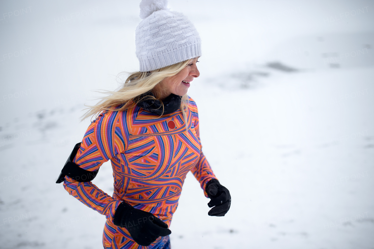 Side view of active senior woman running outdoors in winter, doing exercise.