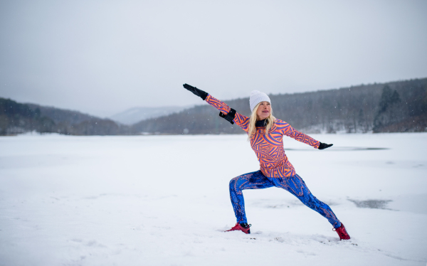 Front view of an active senior woman doing stretching exercise outdoors in winter.