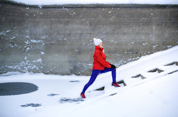 Side view of active senior woman outdoors in snowy winter, doing exercise.