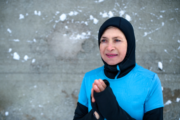 Portrait of an active senior woman standing against wall outdoors in snowy winter. Copy space.