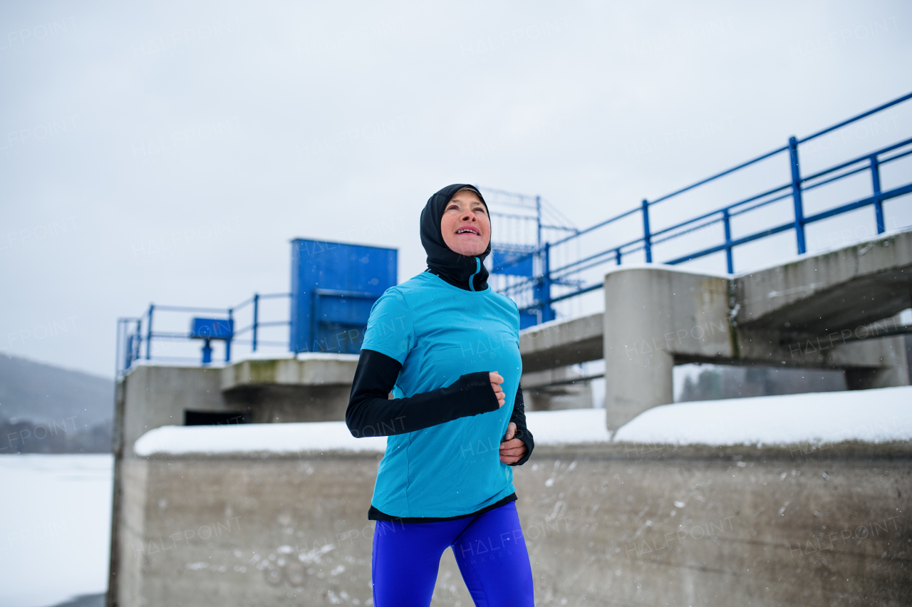 Happy active senior woman running outdoors in snowy winter, cold weather concept.