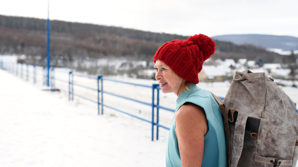 An active senior woman in swimsuit with backpack outdoors in winter, cold therapy concept.