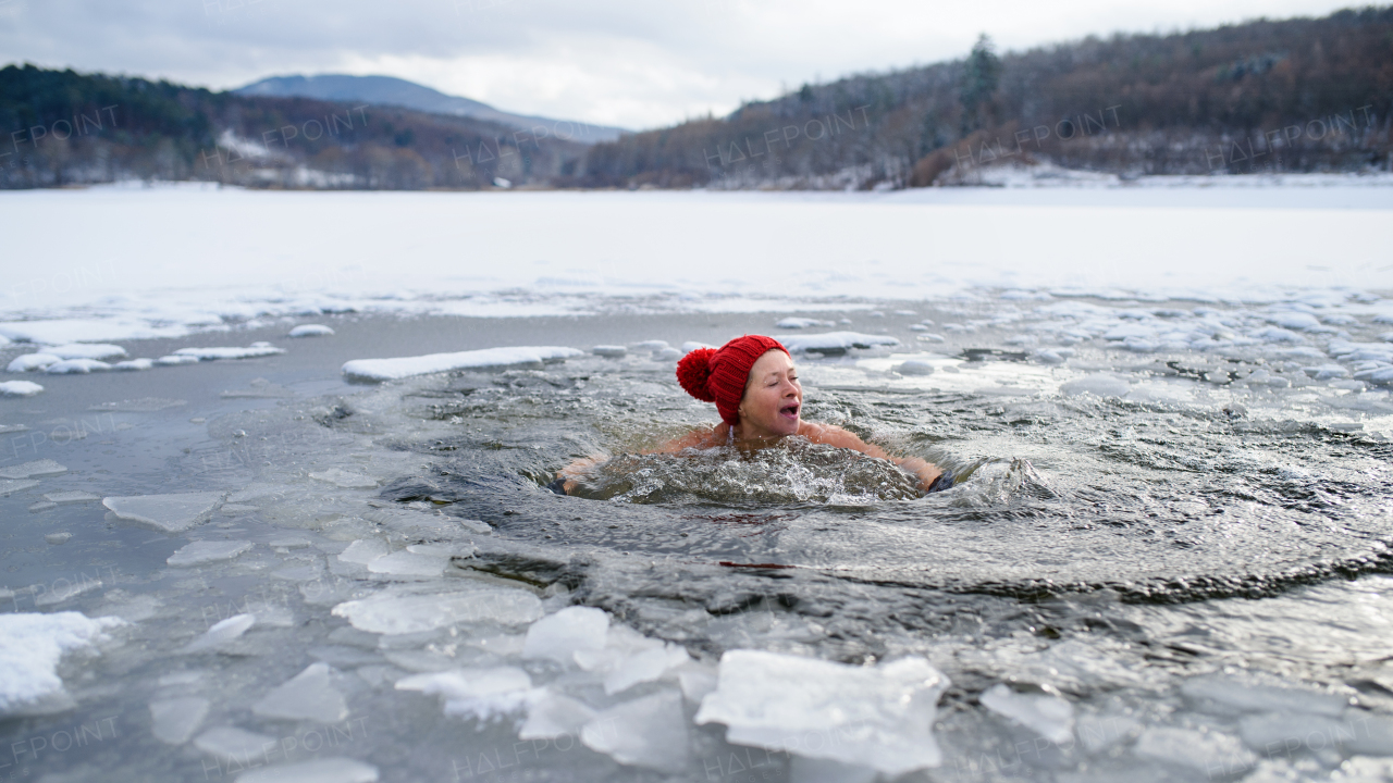 A front view of active senior woman in swimsuit outdoors in water in winter, cold therapy concept.