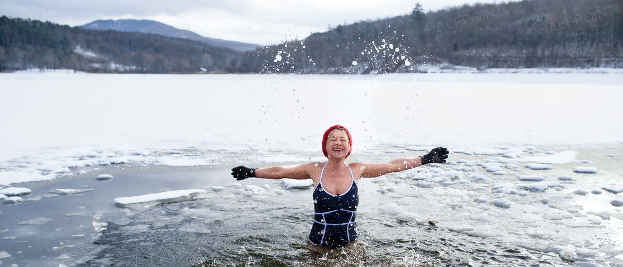 A front view of active senior woman in swimsuit outdoors in water in winter, cold therapy concept.