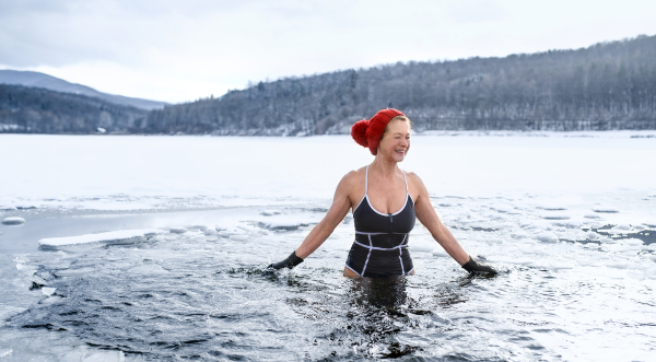 A front view of active senior woman in swimsuit outdoors in water in winter, cold therapy concept.