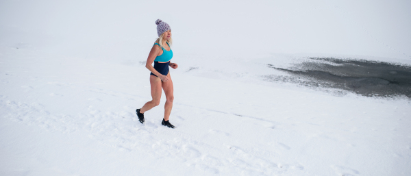 Happy active senior woman in swimsuit running outdoors in winter, cold therapy concept.