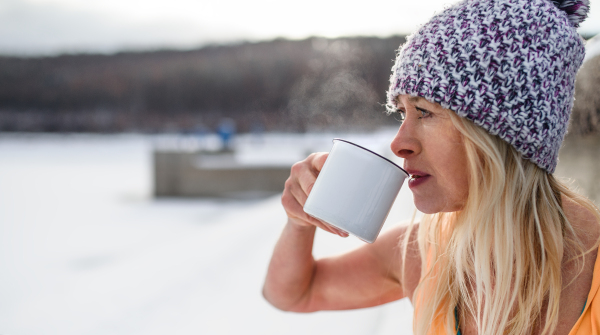 A portrait of active senior woman sports clothes drinking tea outdoors in winter, cold therapy concept. Copy space.