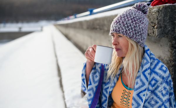 A portrait of active senior woman sports clothes drinking tea outdoors in winter, cold therapy concept. Copy space.