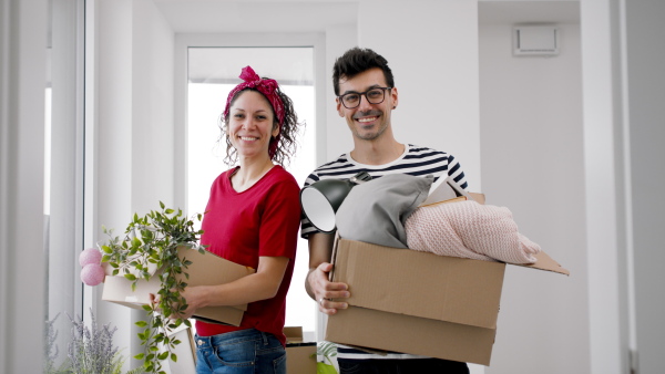 Happy young couple with boxes moving in new flat, looking at camera. New home and relocation concept.