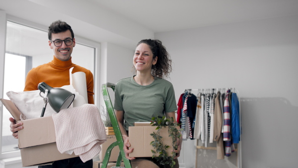 Happy young couple with boxes moving in new flat, looking at camera. New home and relocation concept.