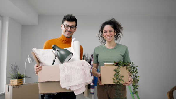 Happy young couple with boxes moving in new flat, looking at camera. New home and relocation concept.