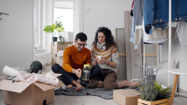 Happy young couple with boxes moving in new flat, having coffee. New home and relocation concept.