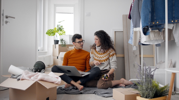 Happy young couple with boxes and laptop moving in new flat, planning. New home and relocation concept.