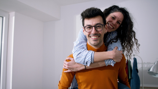 Happy young couple owners in new flat, moving in, doing piggy ride. New home and relocation concept.