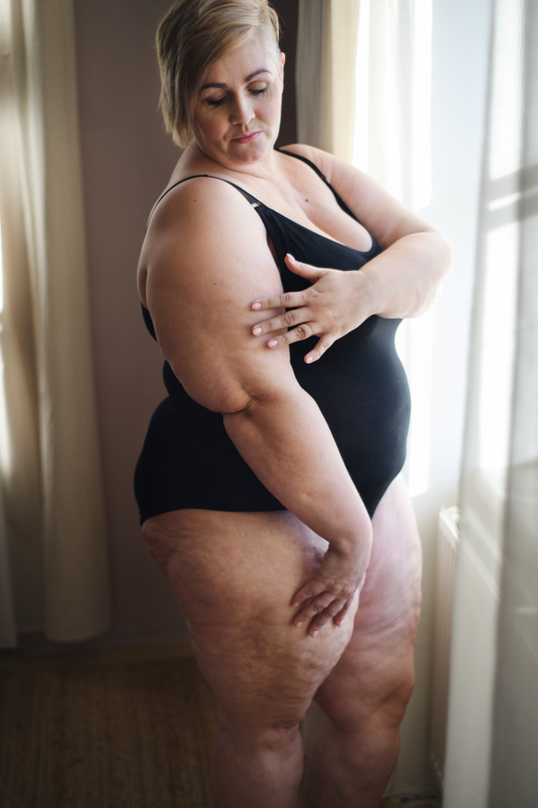 A lonely fat woman standing by the window at home.