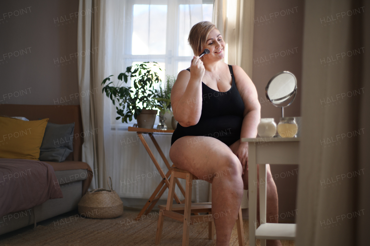 An overweight woman sitting and applying make up at home, selfcare concept.