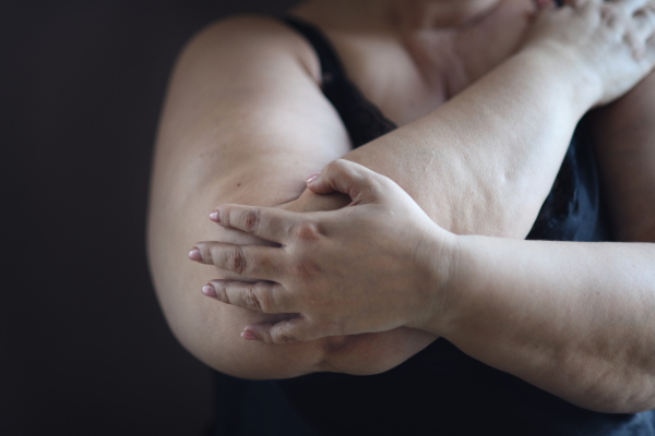 Close up for an obese woman body sitting and looking through the window at home.