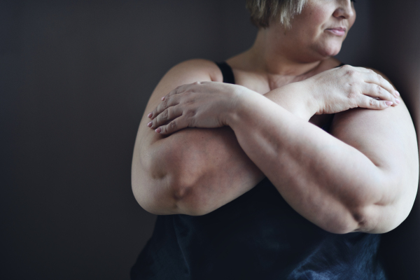 A depressed fat woman standing with arms crossed and looking through the window at home, cut out