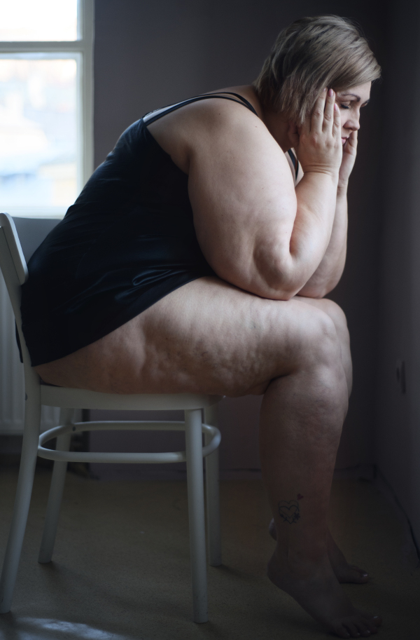 Depressed lonely fat woman sitting and looking through the window at home at dark.