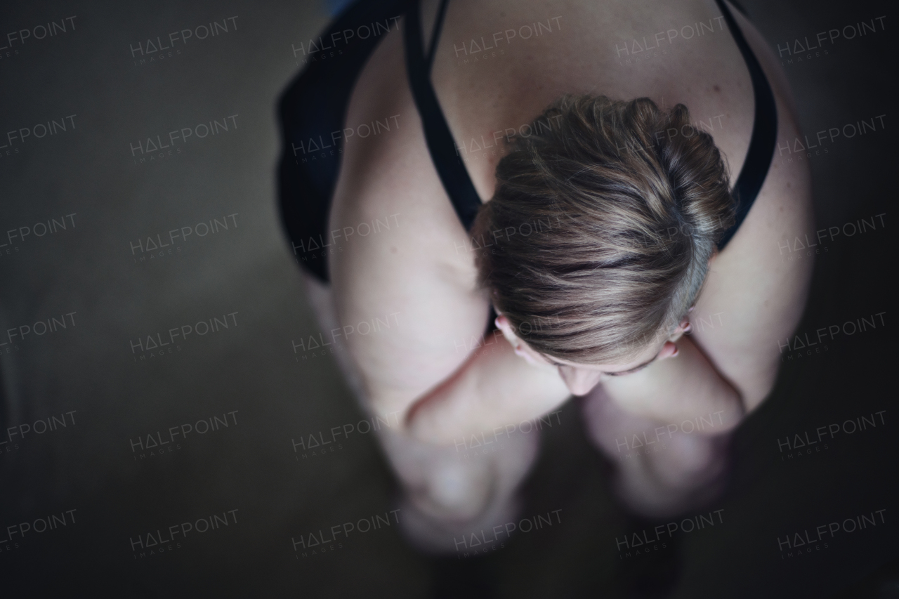 An overhead view of depressed lonely fat woman sitting and looking through the window at home.