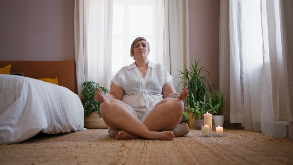 An overweight woman meditating at home.