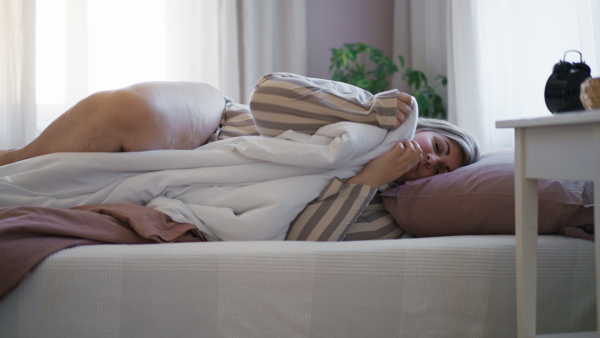 An overweight woman waking up in bed and switching off the alarm clock at home.