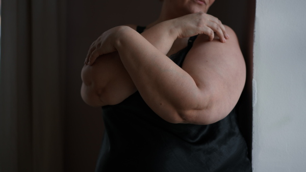 A depressed fat woman standing with arms crossed and looking through the window at home, cut out