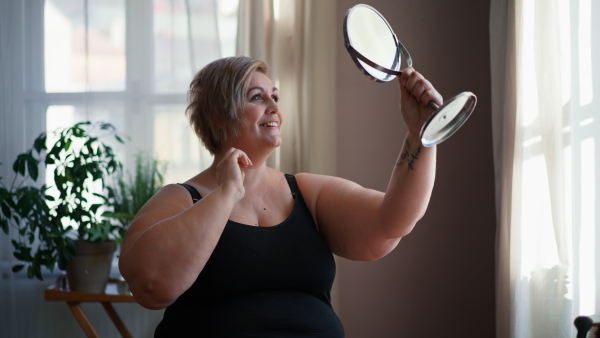 A fat woman sitting and looking at mirror at home, selfcare concept.