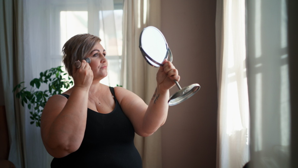 A fat woman sitting and looking at mirror at home, selfcare concept.