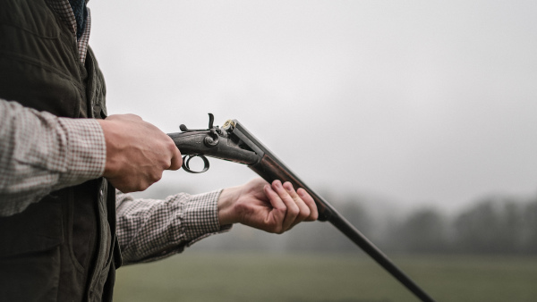 A close-up of hunter man charges the cartridge on rifle gun in forest.