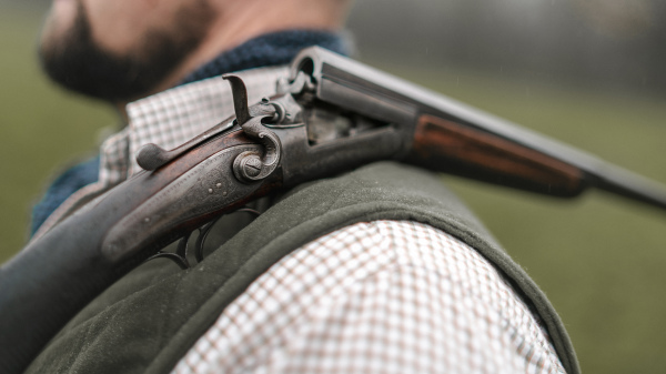 A close-up of unter man in traditional shooting clothes with shotgun on his shoulder.