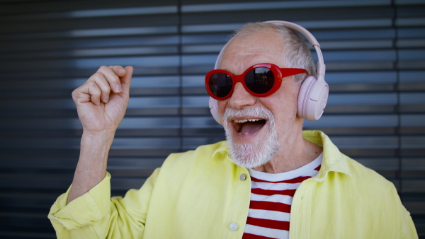 Crazy senior man with sunglasses and headphones listening to music and having fun.