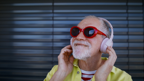 Crazy senior man with sunglasses and headphones listening to music and having fun.