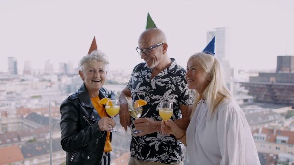 Front view of group of senior friends having party outdoors on balcony and looking at camera.