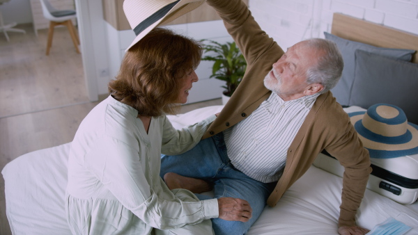 A senior couple arriving in hotel room, sitting on bed and having fun. Holiday a concept.