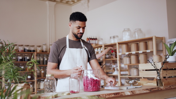 A young man filling jar by dryed raspberries in zero waste shop.