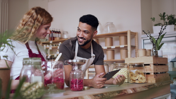 Young colleagues filling jar by dryed raspberries and talking in zero waste shop.