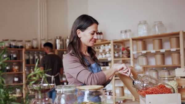 Young woman filling paper bag by pasta in zero waste shop.