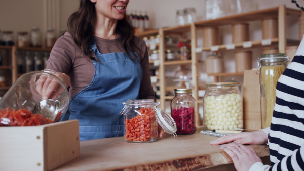 Young woman with curly hair buying fresh pasta in zero waste shop.