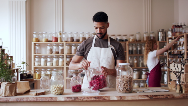 A young man filling jar by dryed raspberries in zero waste shop.