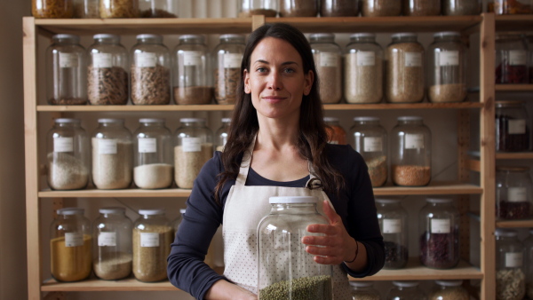 Young female owner of zero waste shop holding jar looking at camera.